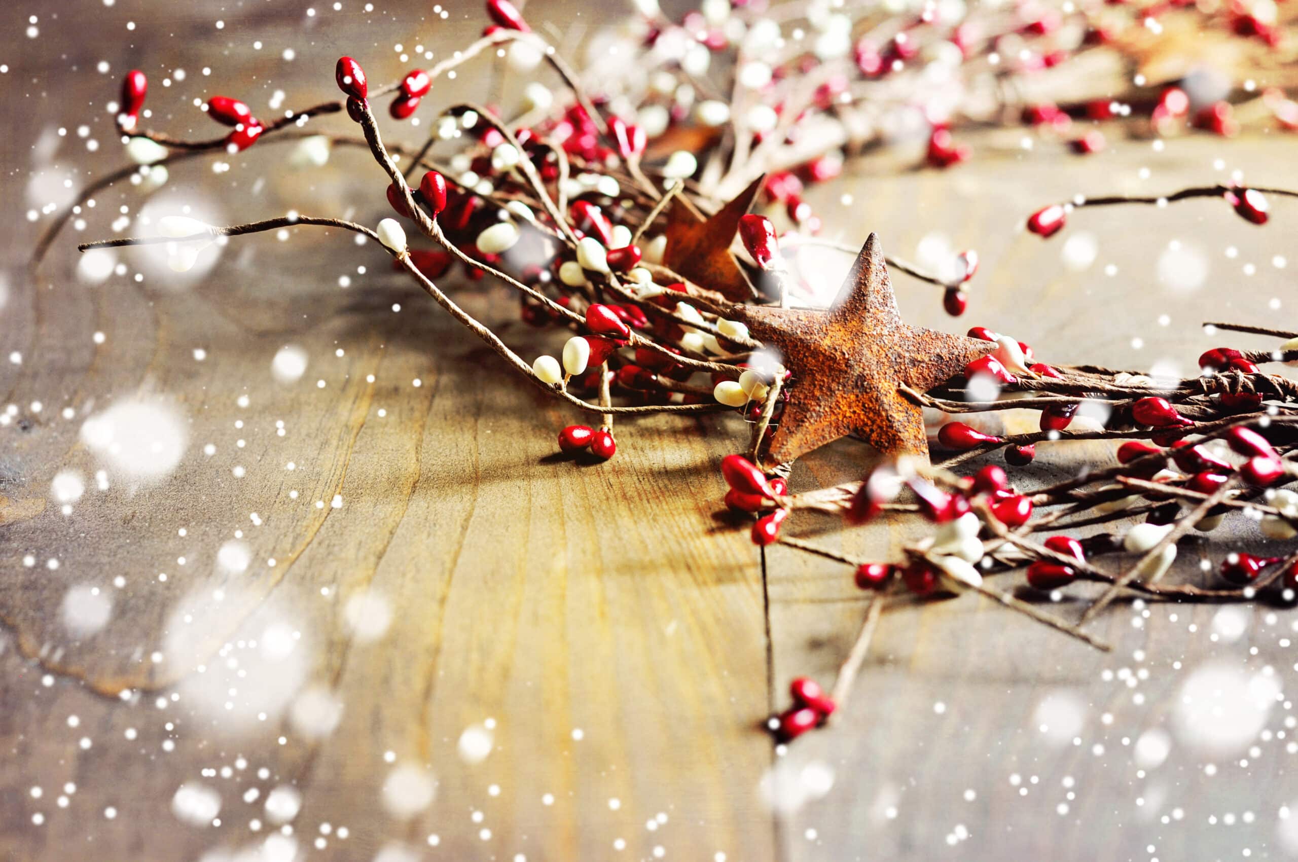 Christmas wreath with red and white berries and rusty metal stars on wooden background. Falling snow effect. Vintage Style