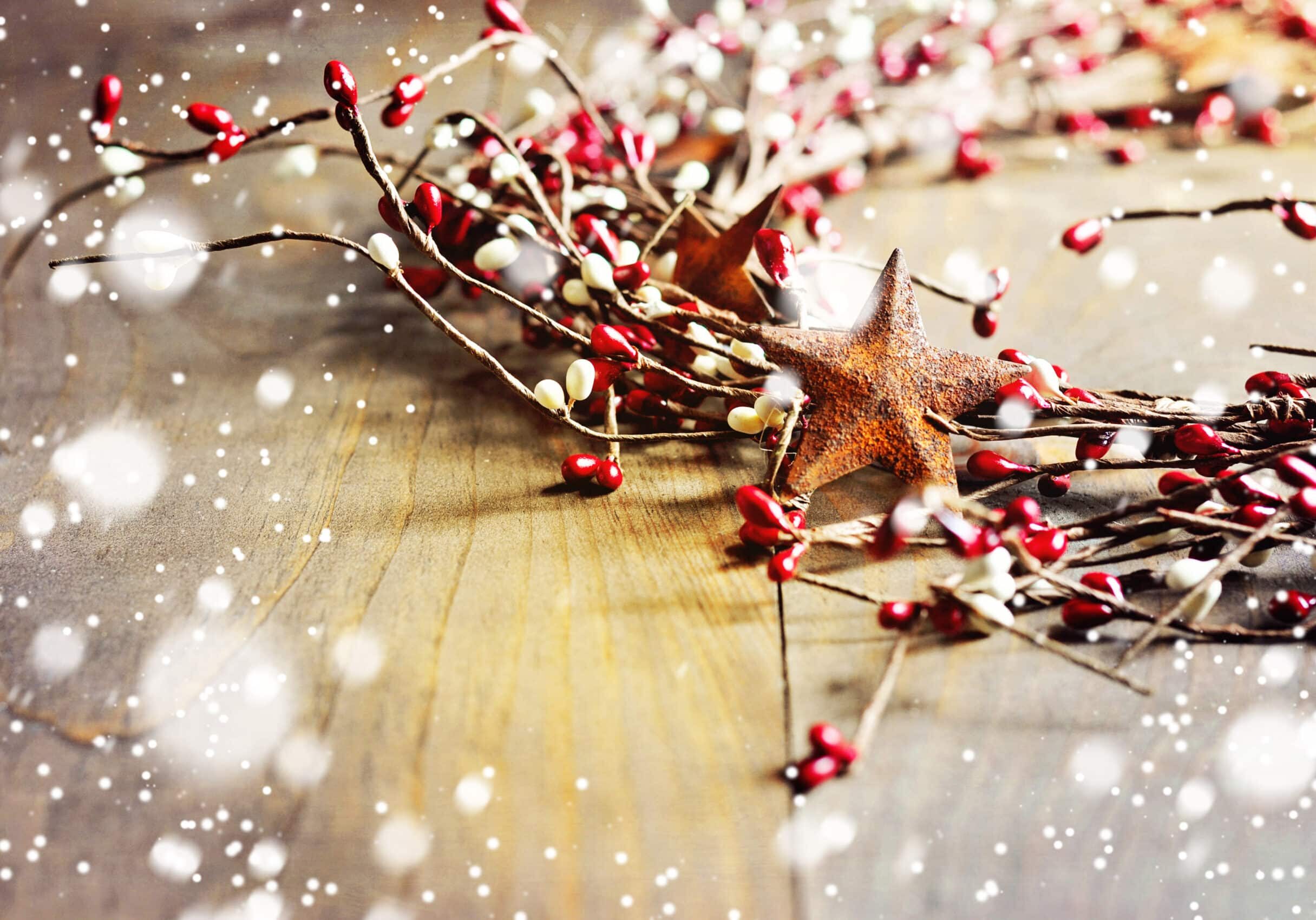 Christmas wreath with red and white berries and rusty metal stars on wooden background. Falling snow effect. Vintage Style